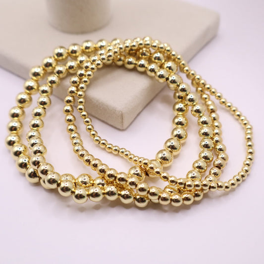 Close-up of four stacked 18K gold filled bead bracelets on a display stand, showcasing smooth polished finish and uniform design.