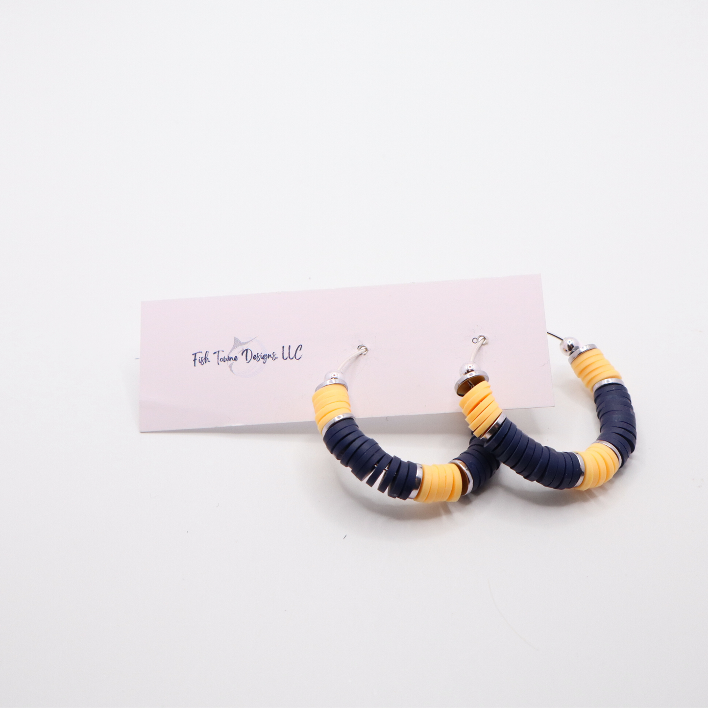 Navy and gold heishi bead hoop earrings with gold accents hanging on a minimalist jewelry stand against a white background