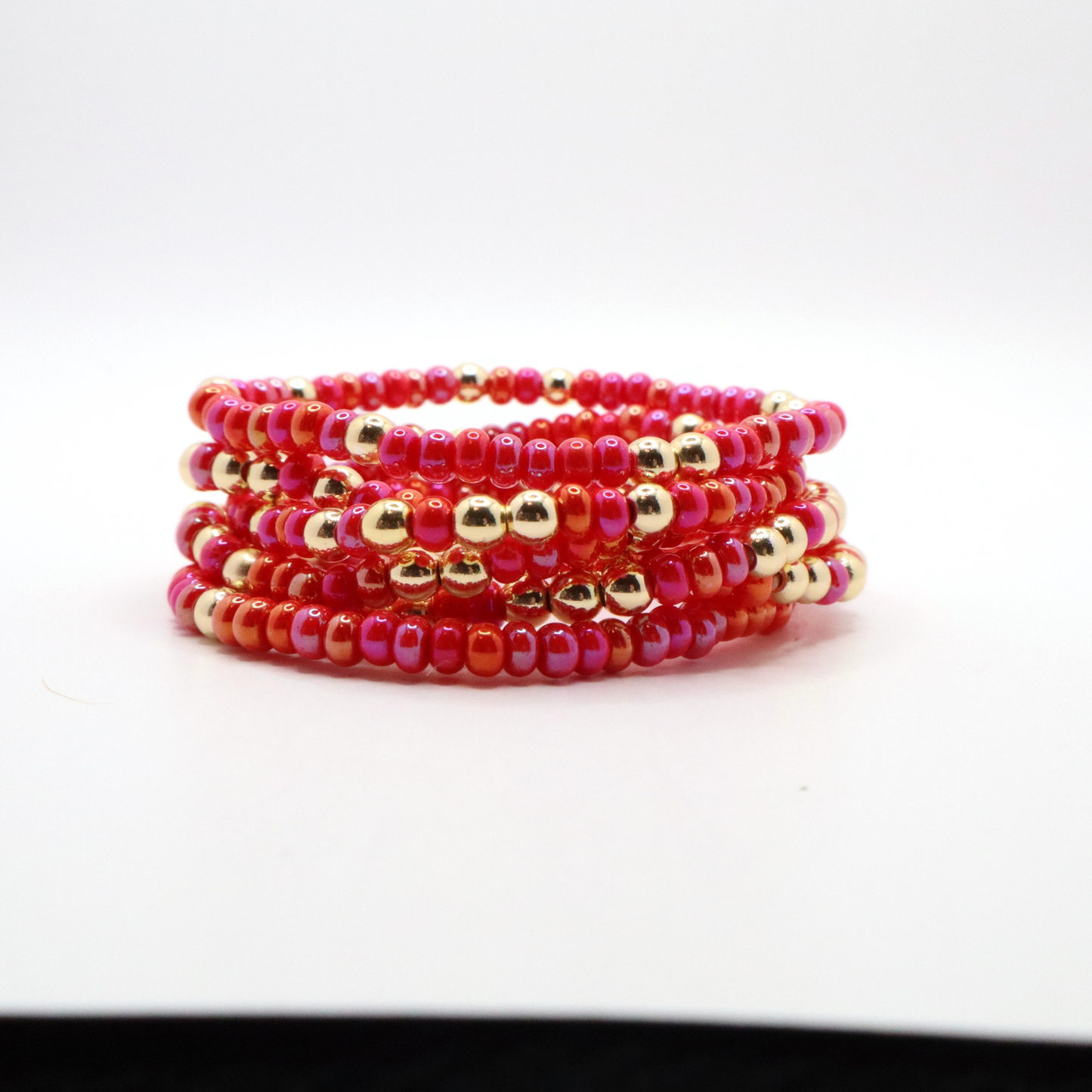 Stack of six pink and gold beaded bracelets on a white background