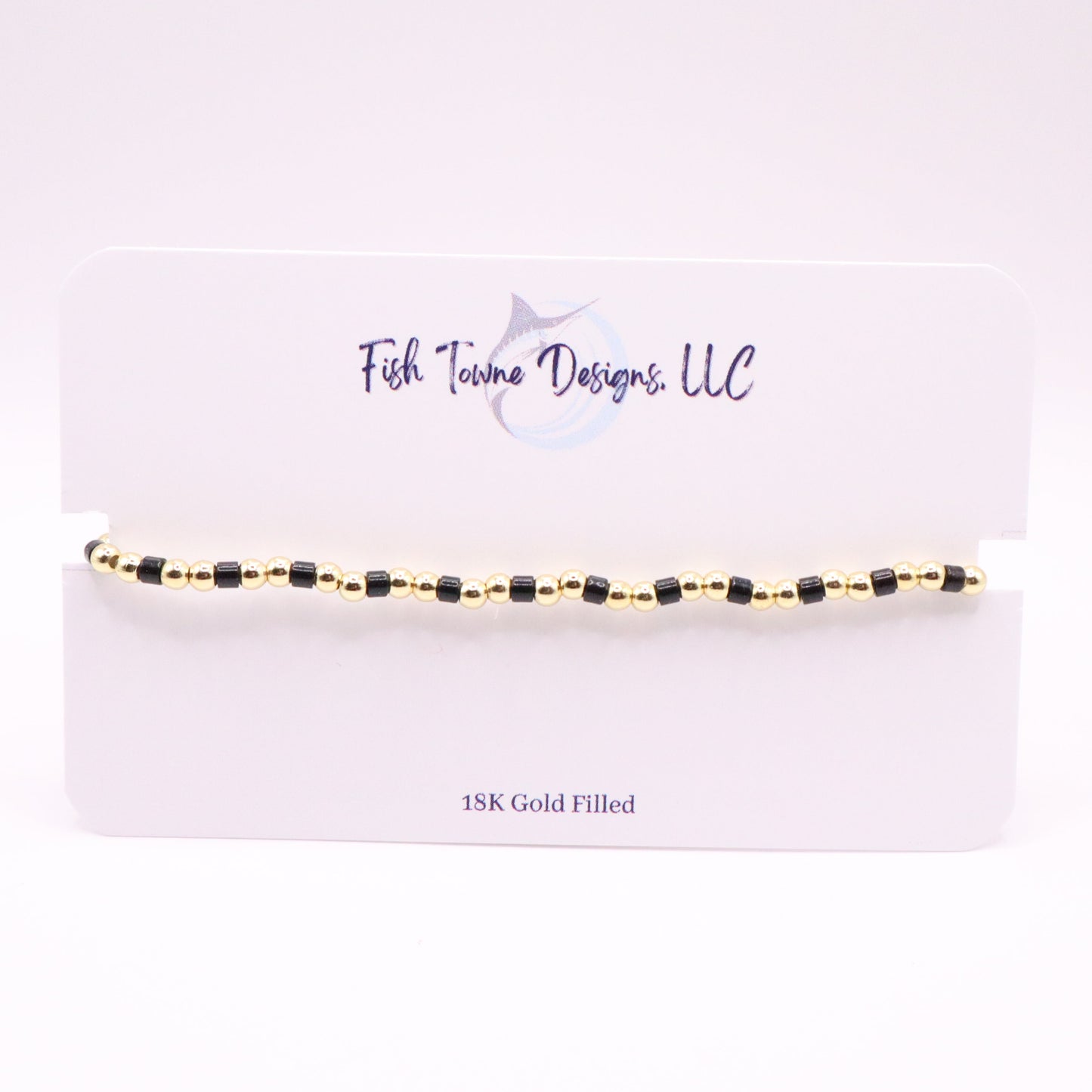 Gold and black beaded bracelet on a white card with 'Fish Towne Design, LLC' branding.