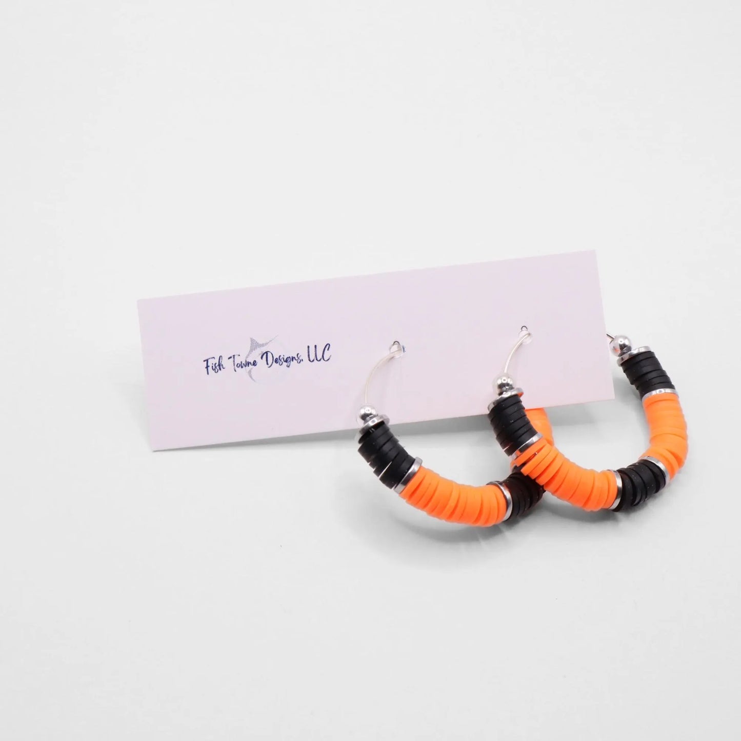 Orange and black heishi bead hoop earrings with silver accents displayed on a branded card against a clean white background
