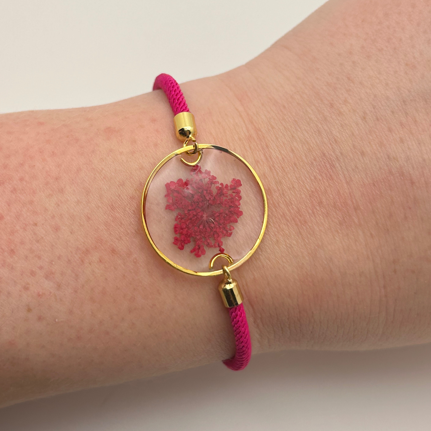 Bracelet with pink cord and gold clasp featuring a pink floral design on a wrist.