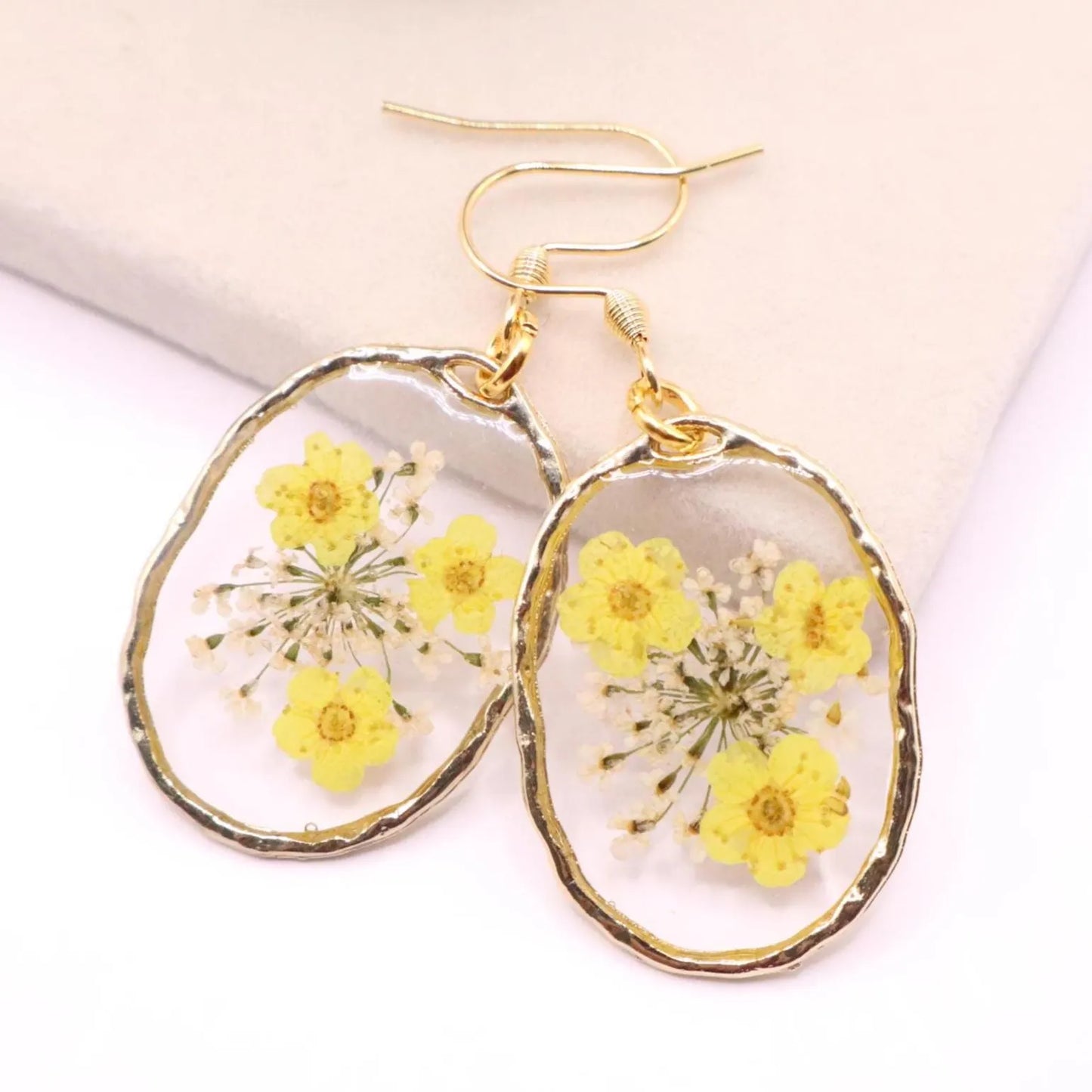 Real flower resin dangle earrings with yellow pressed flowers in clear resin framed in gold with gold hook ear wires on display