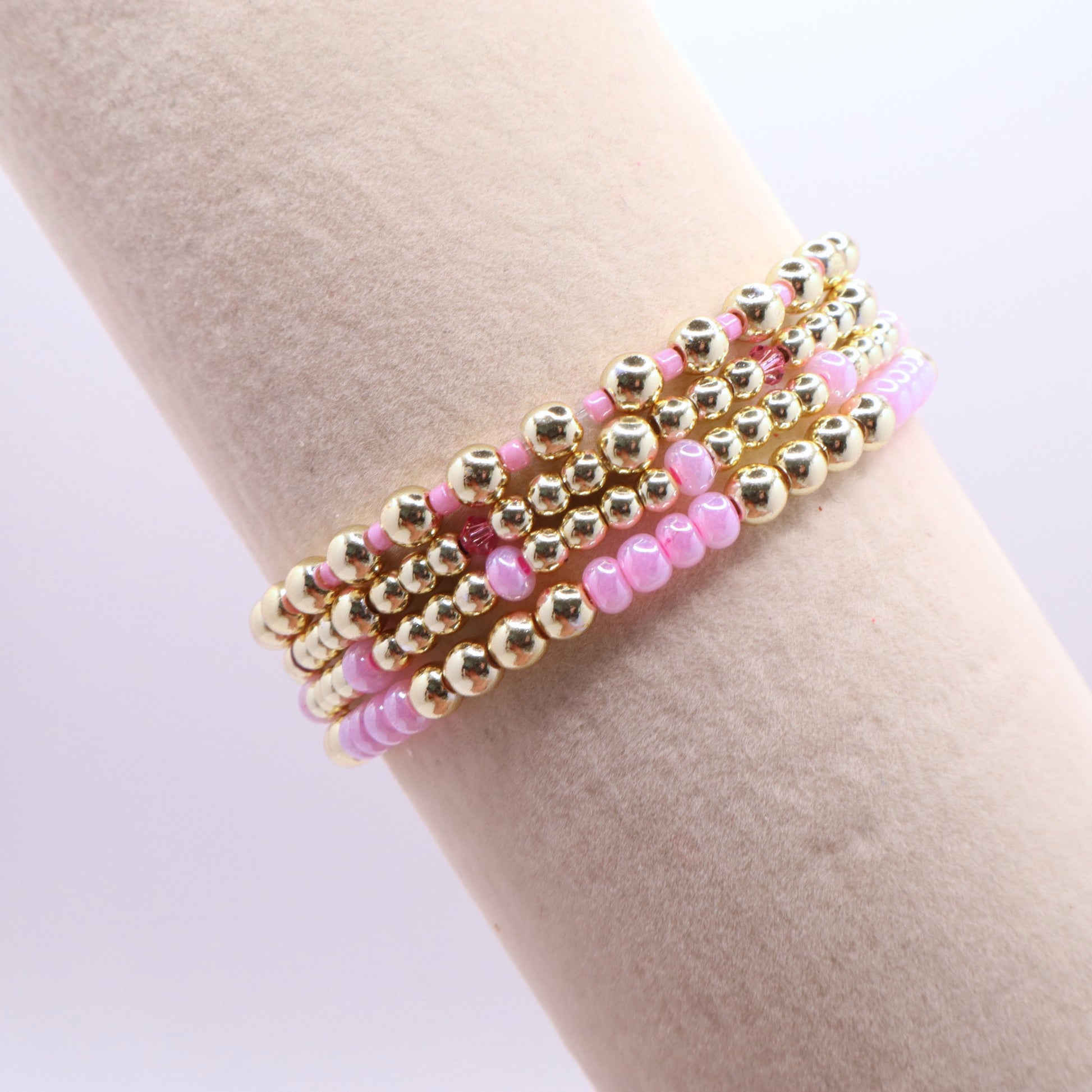 Three-piece pink hematite bracelet stack featuring gold-tone beads and soft pink glass accents.