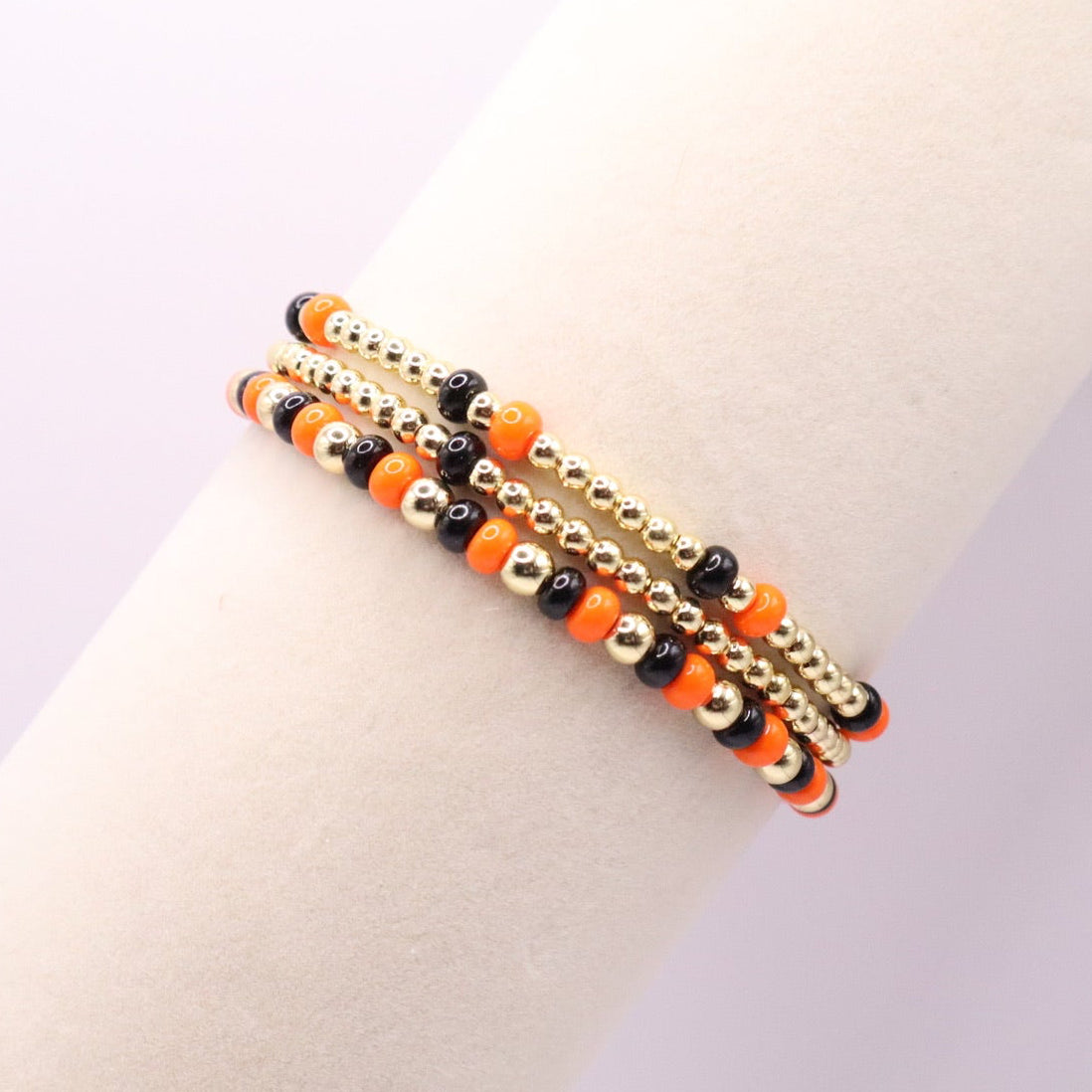 Three orange, black and gold bracelets on a bracelet display