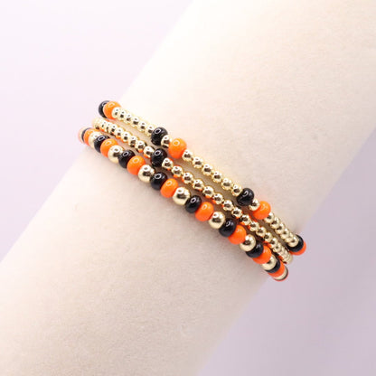 Three orange, black and gold bracelets on a bracelet display
