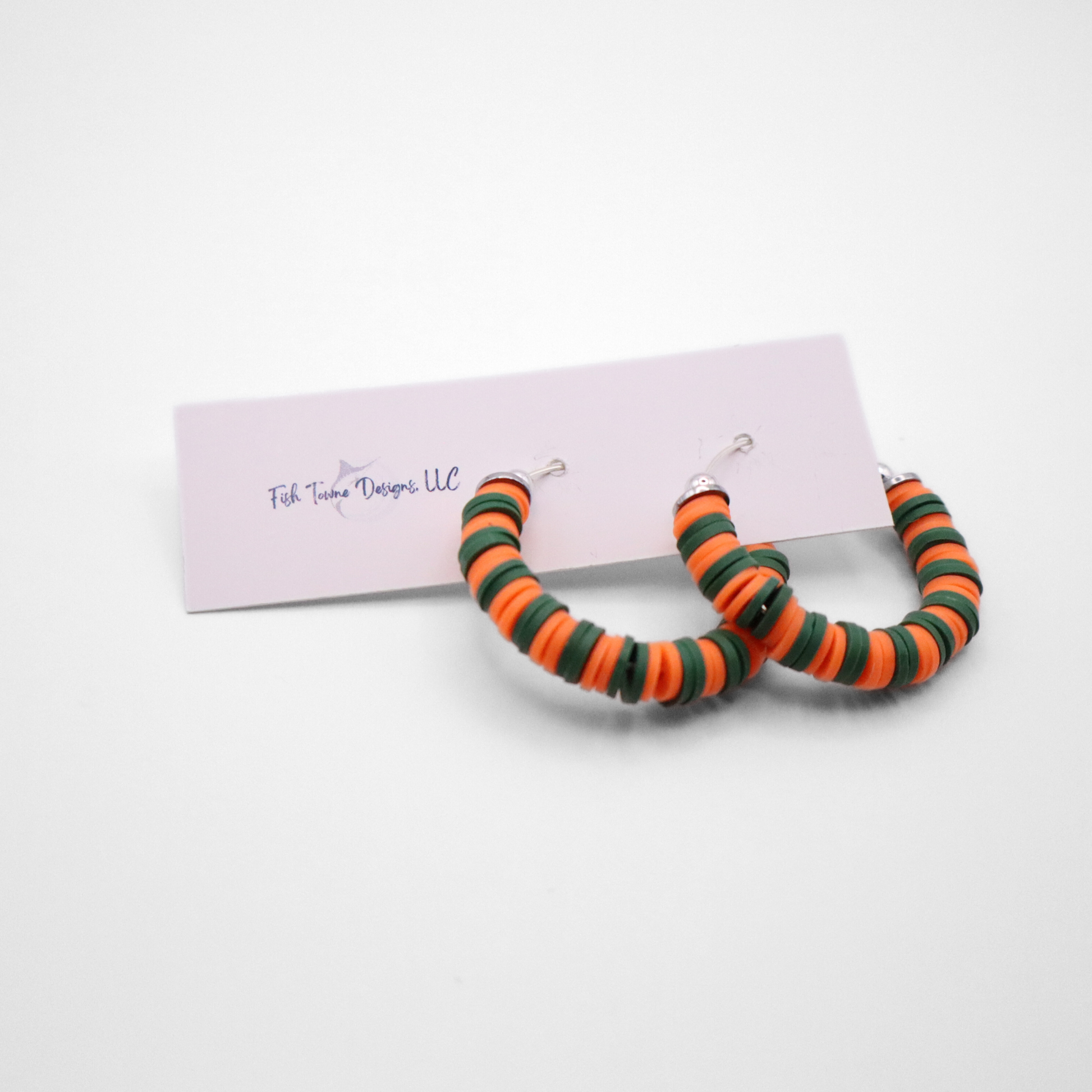 Orange and green heishi bead hoop earrings with silver accents displayed on a branded card against a white background
