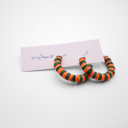 Orange and green heishi bead hoop earrings with silver accents displayed on a branded card against a white background