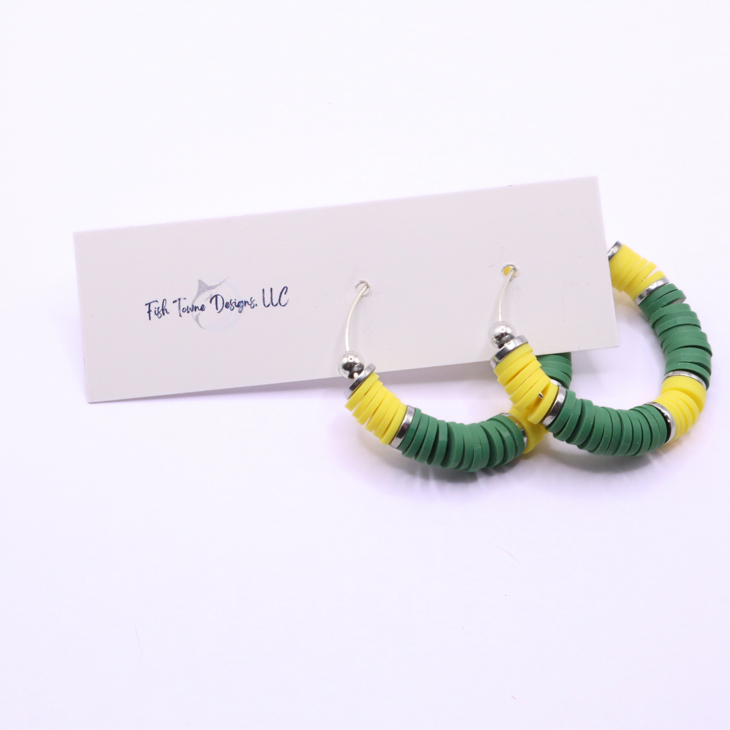 Green and yellow heishi bead hoop earrings with silver accents displayed on a branded card against a clean white background