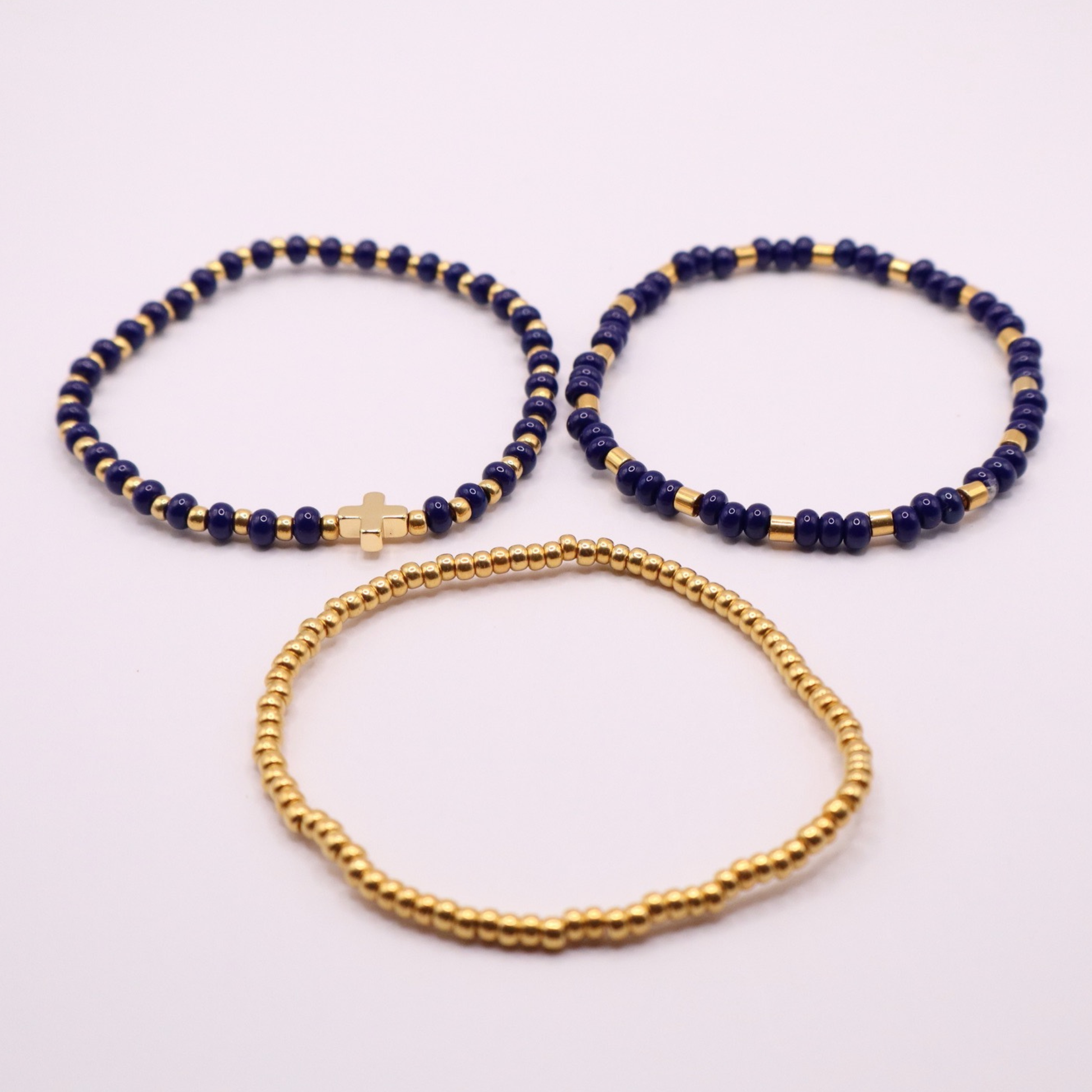 Three gold plated beaded bracelets with gold and navy beads on a white background