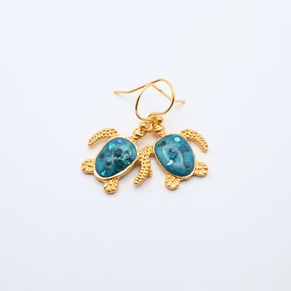 Turtle-shaped earrings with teal blue resin on a white background