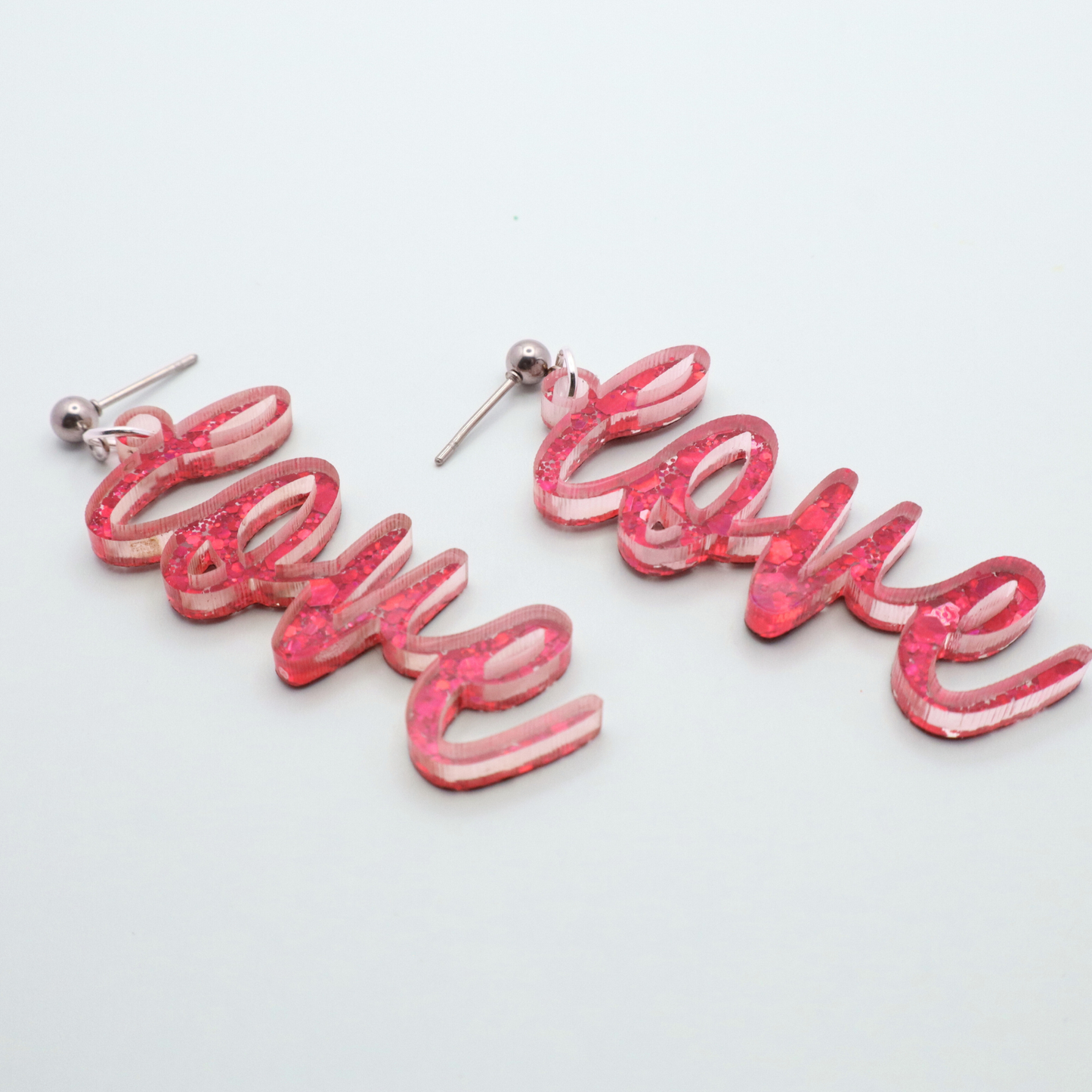 Pink glitter 'love' earrings on a white gray background