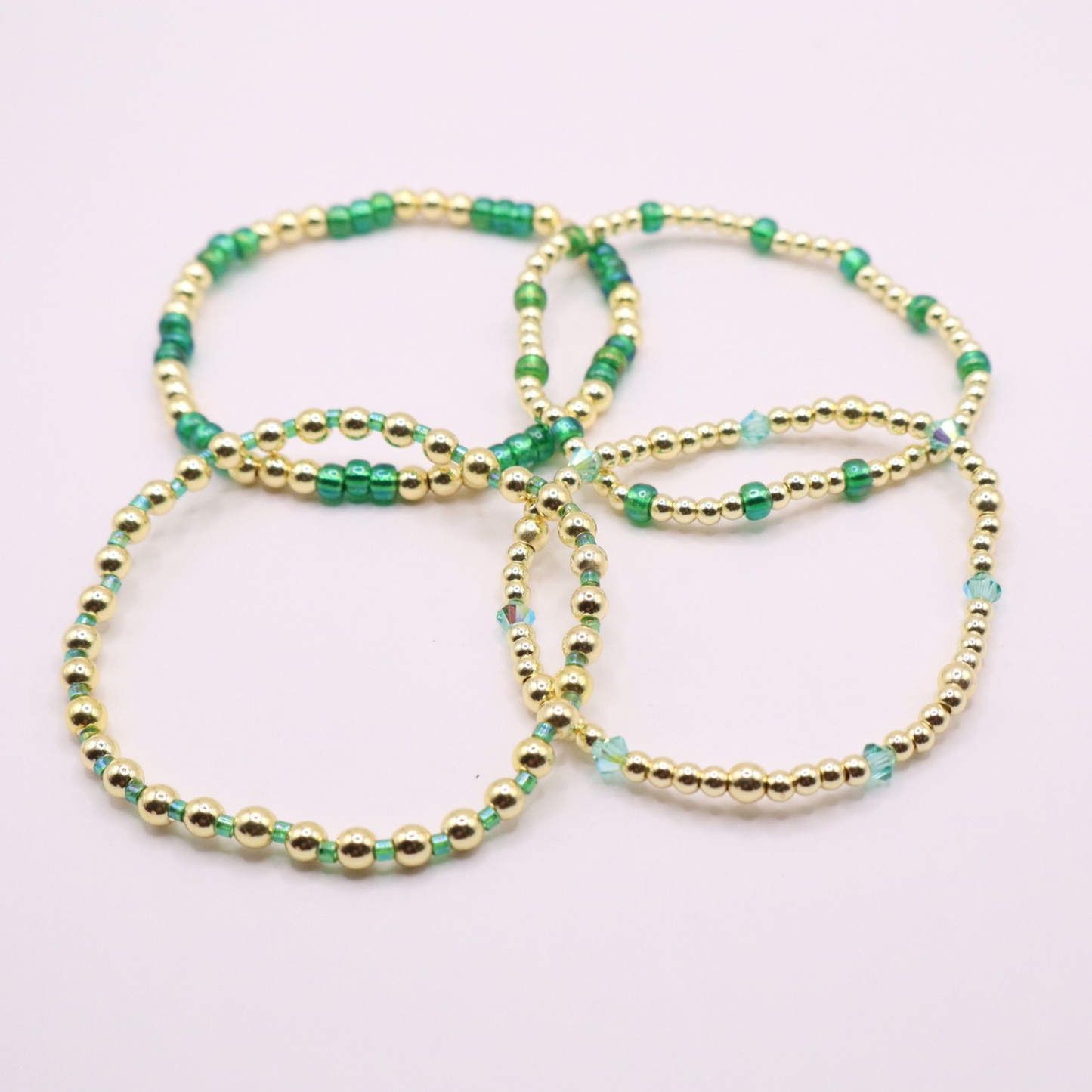 Handmade bracelet stack with green Preciosa seed beads, iridescent crystal accents, and polished gold-tone hematite beads on a clean white background.