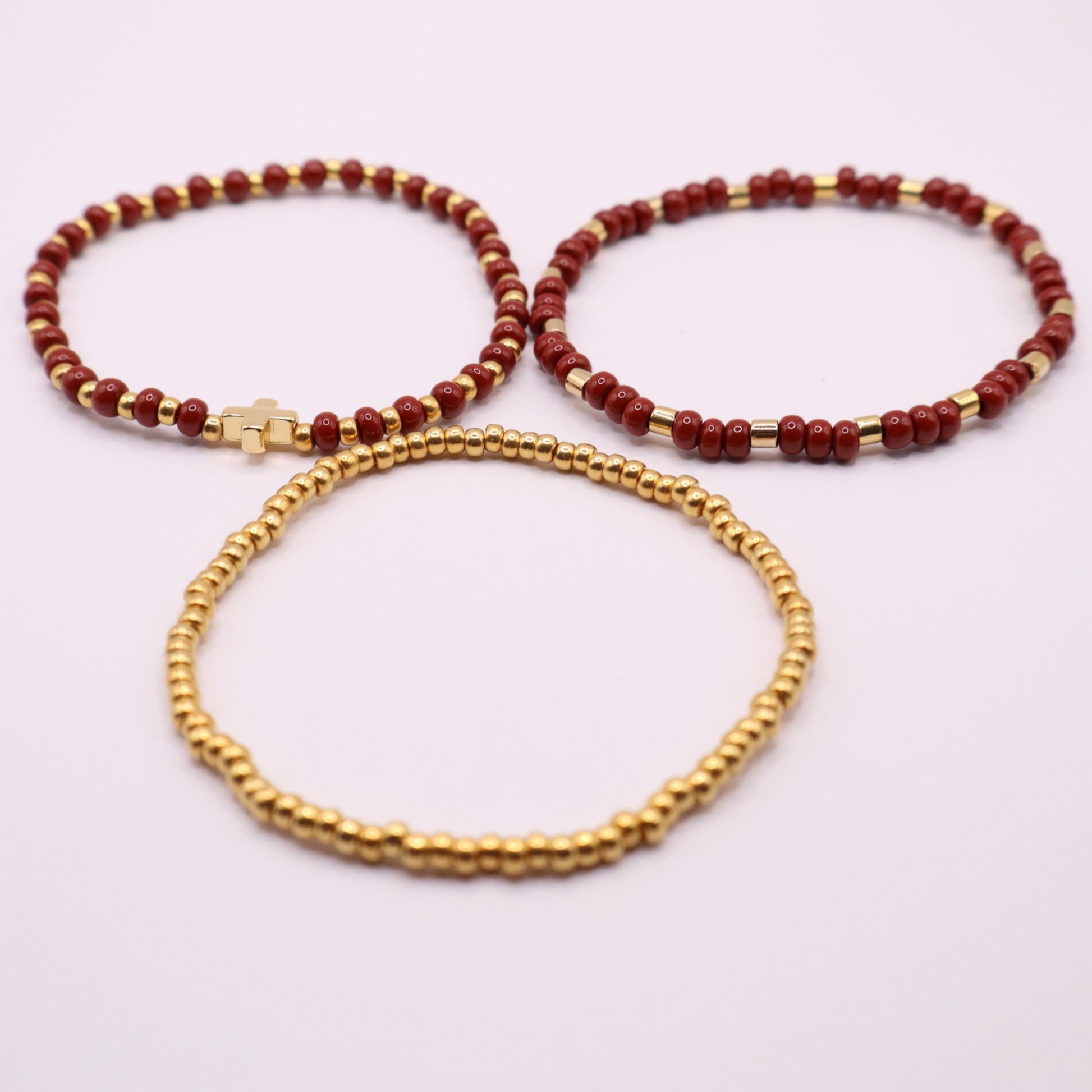 Three beaded bracelets, two red and one gold, on a light pink background