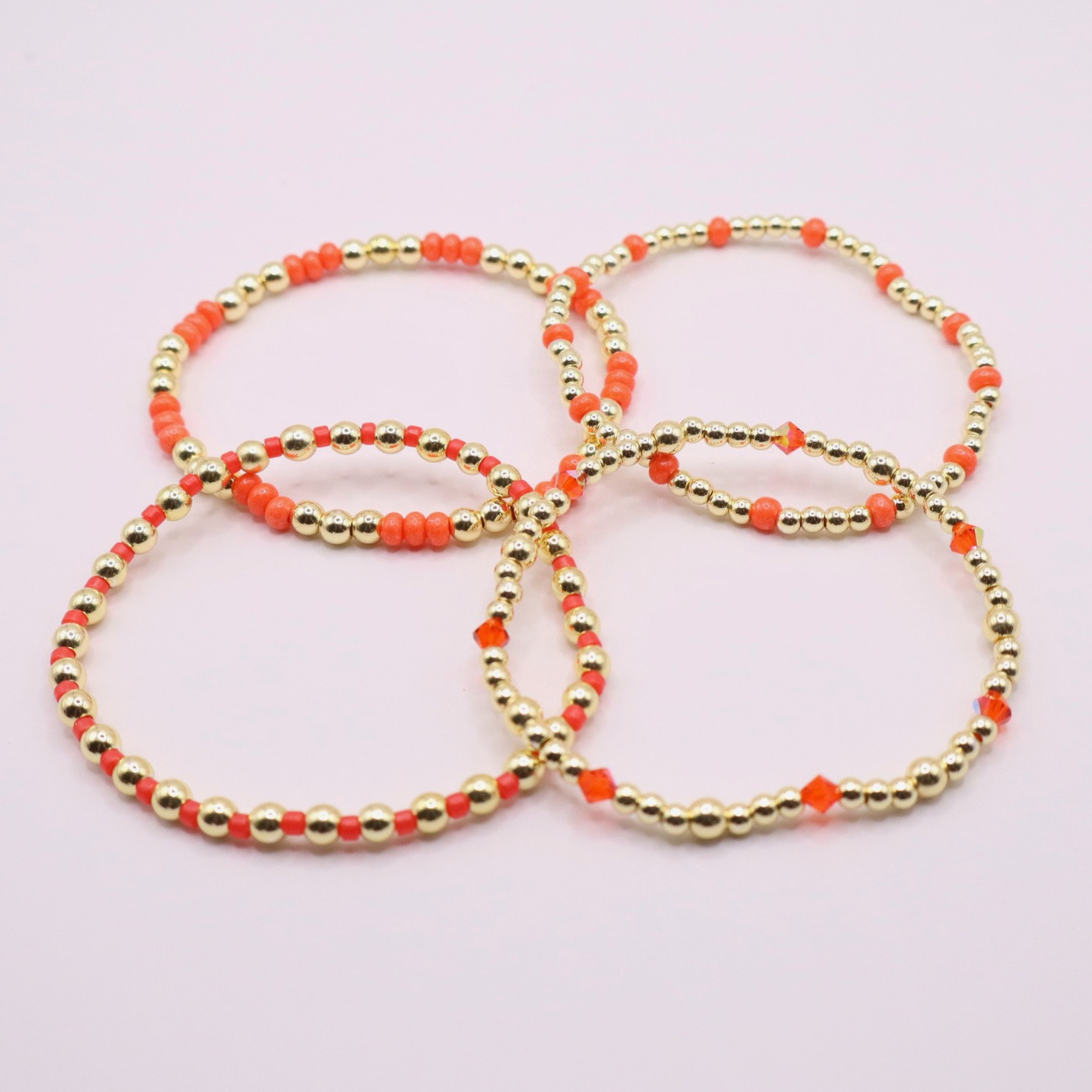 Stack of handmade stretch bracelets featuring vibrant coral Preciosa seed beads, faceted crystal accents, and polished gold-tone hematite beads on a clean white background.