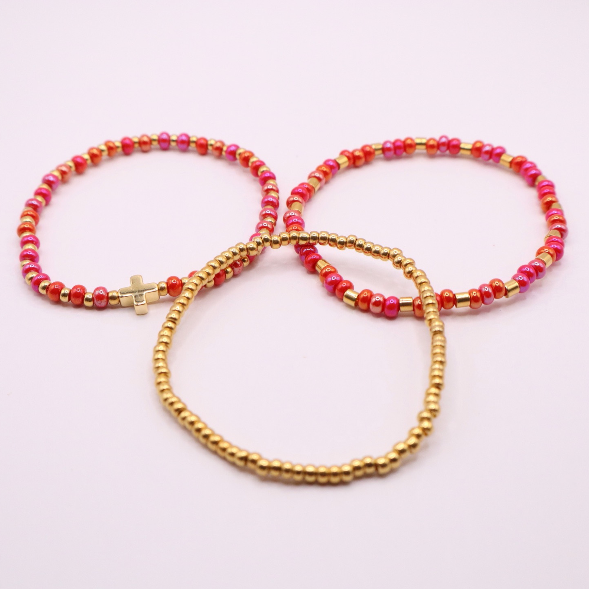 Three beaded bracelets with pink and gold beads on a light pink background