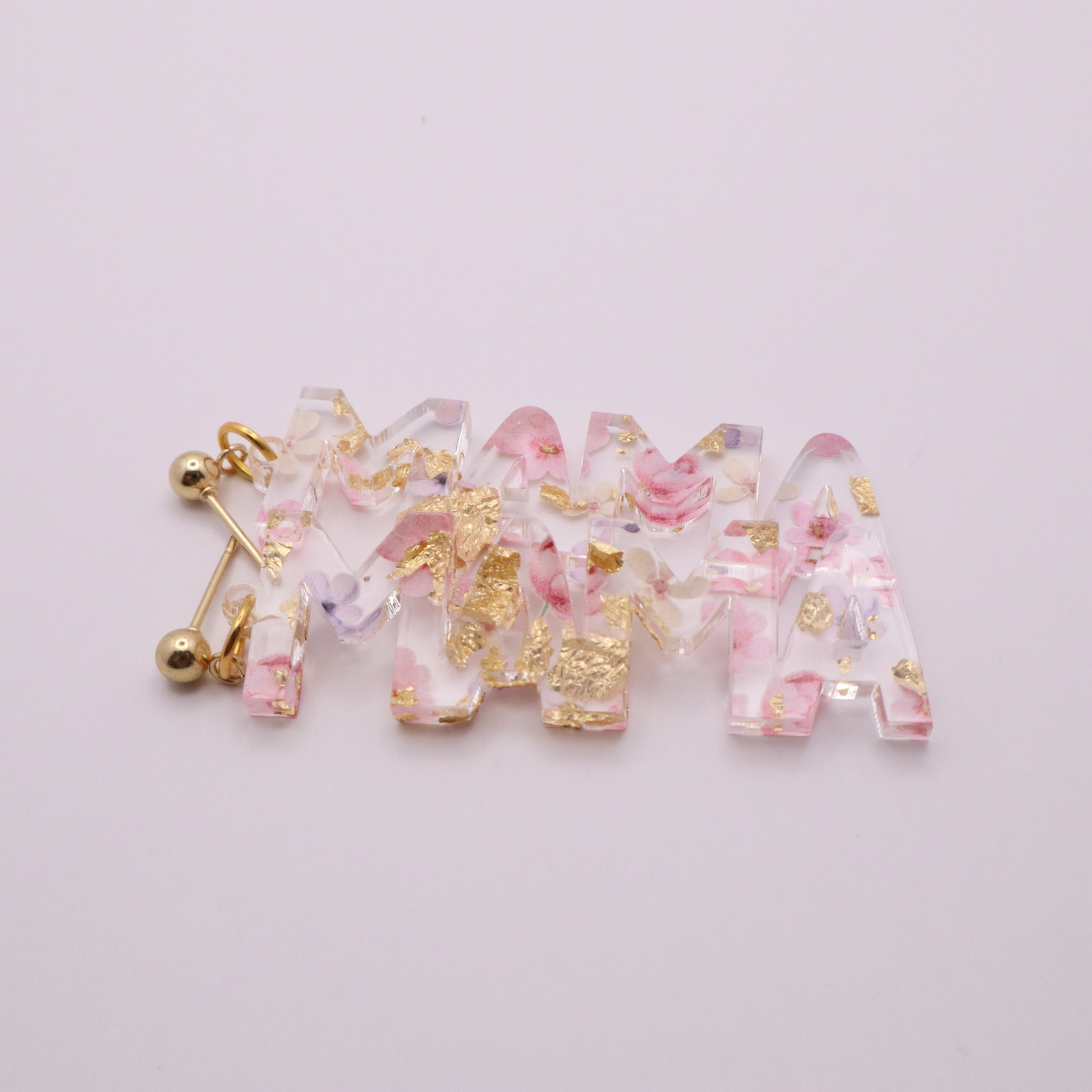 Decorative Mama earrings with floral and gold accents on a light pink background