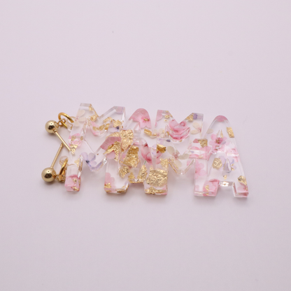 Decorative Mama earrings with floral and gold accents on a light pink background