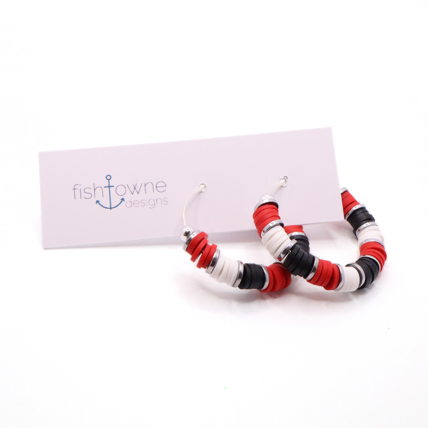Handmade red, white, and black polymer clay heishi bead hoop earrings with silver spacers shown on a white background with display card