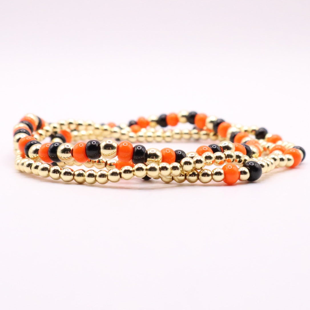 Set of beaded bracelets with gold, black, and orange beads on a white background