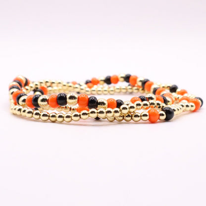 Set of beaded bracelets with gold, black, and orange beads on a white background