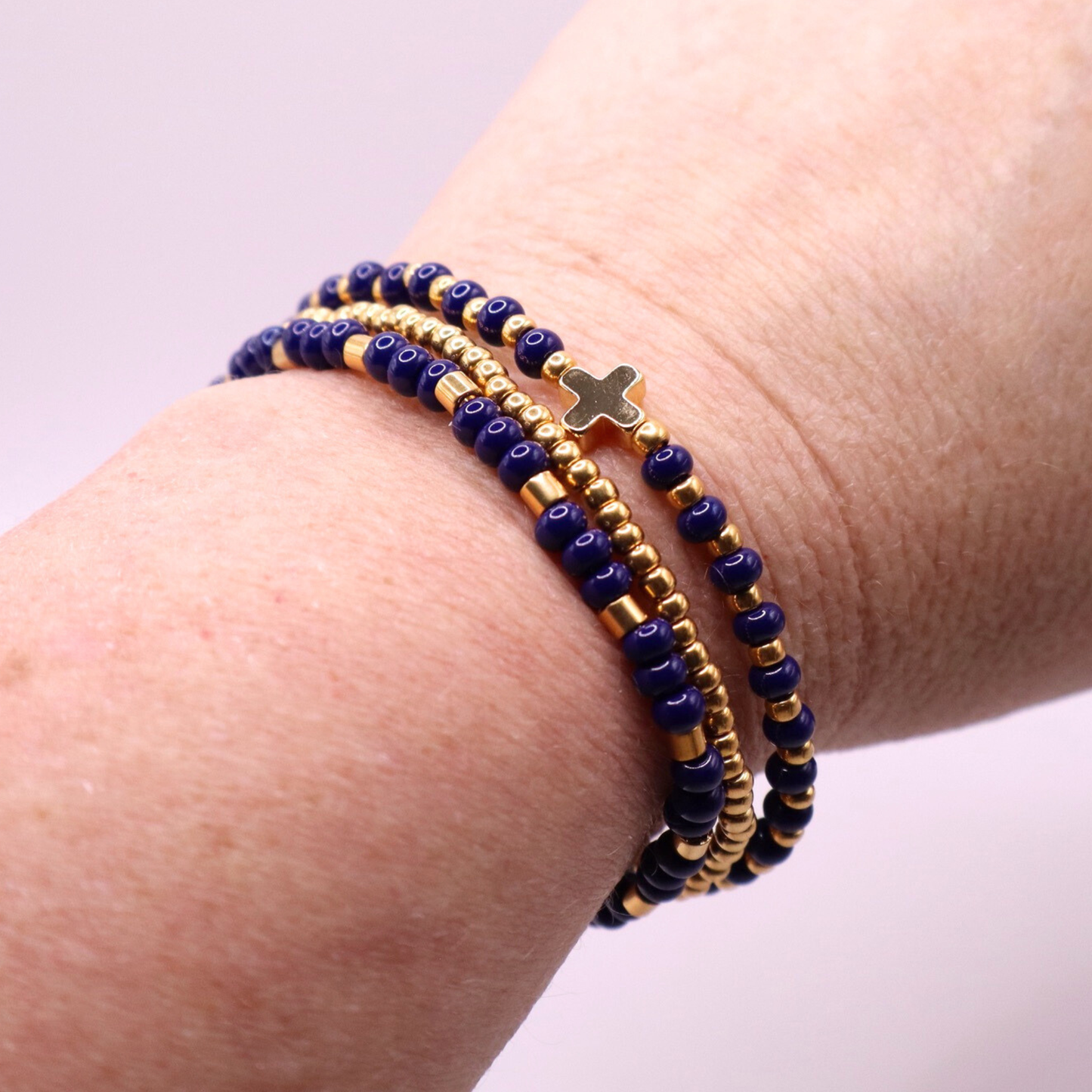 Three beaded bracelets with gold plated and blue beads on a wrist against a light background