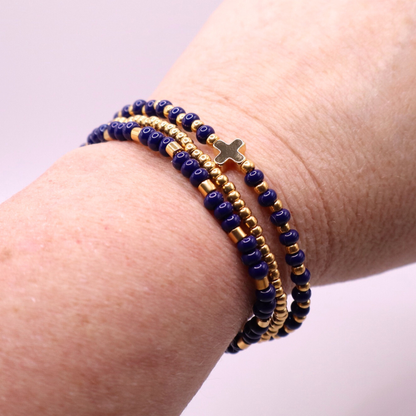 Three beaded bracelets with gold plated and blue beads on a wrist against a light background