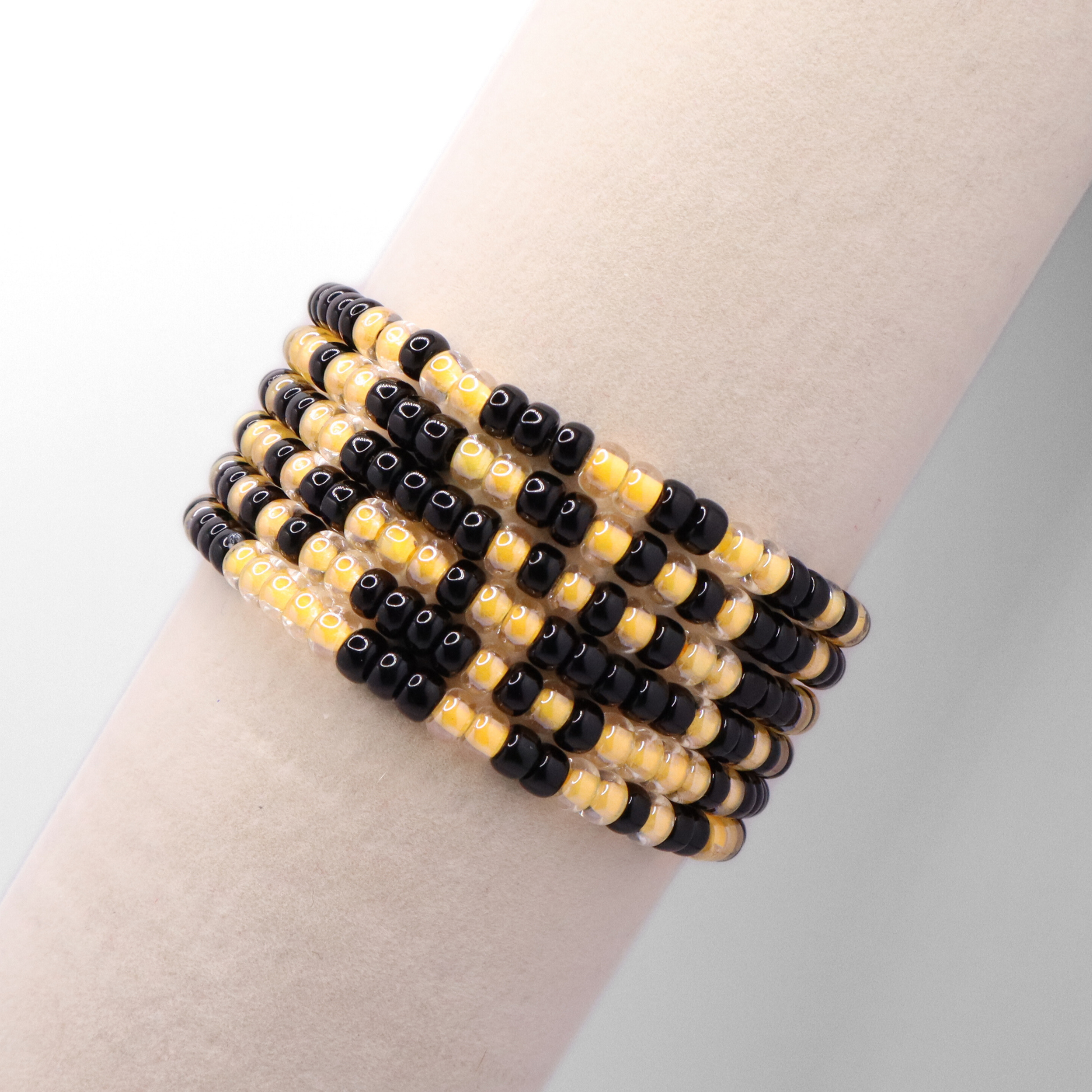 Set of six black and gold seed bead stretch bracelets featuring random black and gold seed beads on a white background