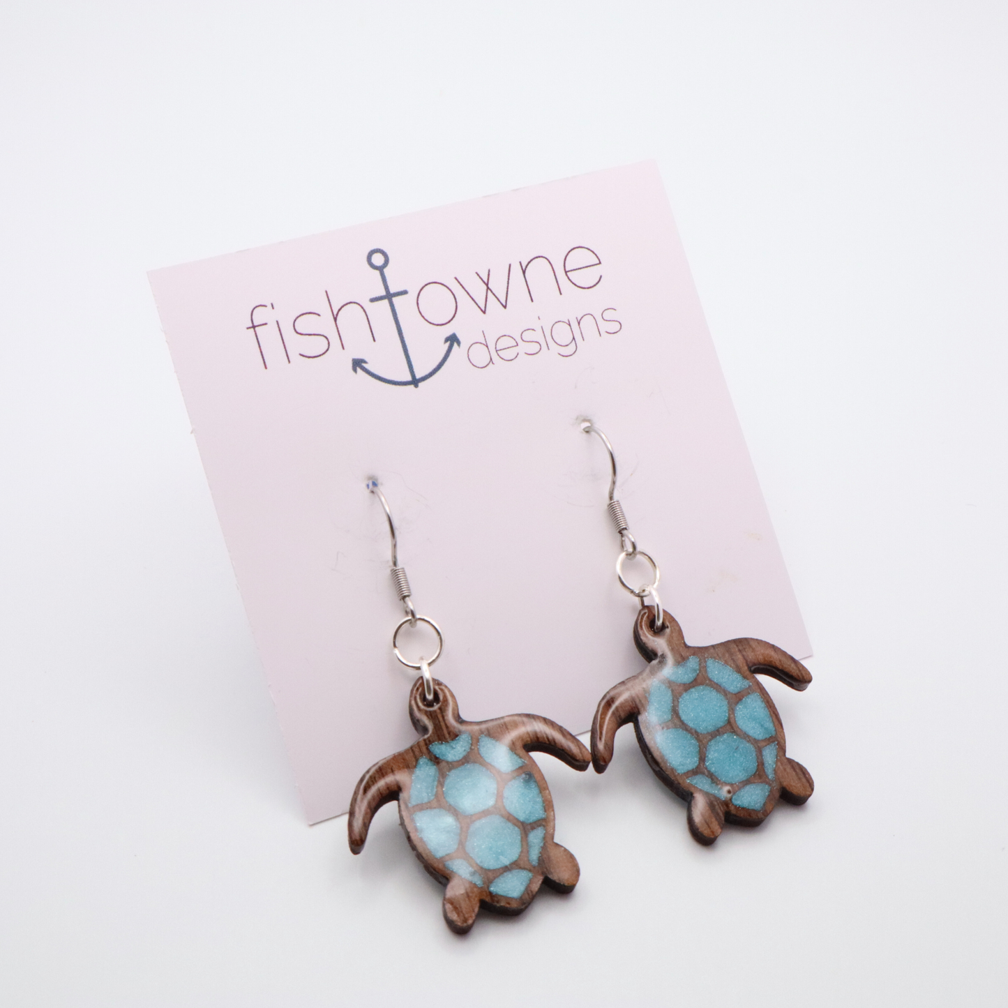 Turtle-shaped earrings with sea glass blue resin hanging on a Fish Towne Designs card.