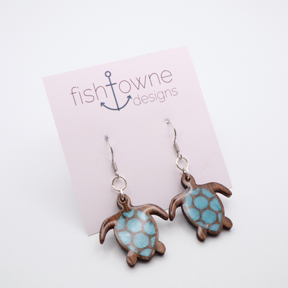 Turtle-shaped earrings with sea glass blue resin hanging on a Fish Towne Designs card.
