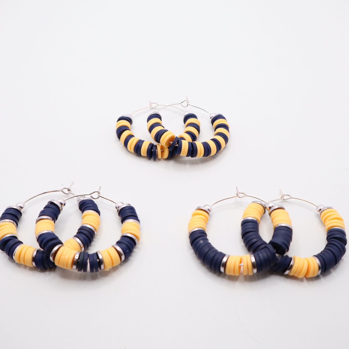 Set of three navy and gold heishi bead hoop earring styles arranged on a white background, showcasing size and pattern variations