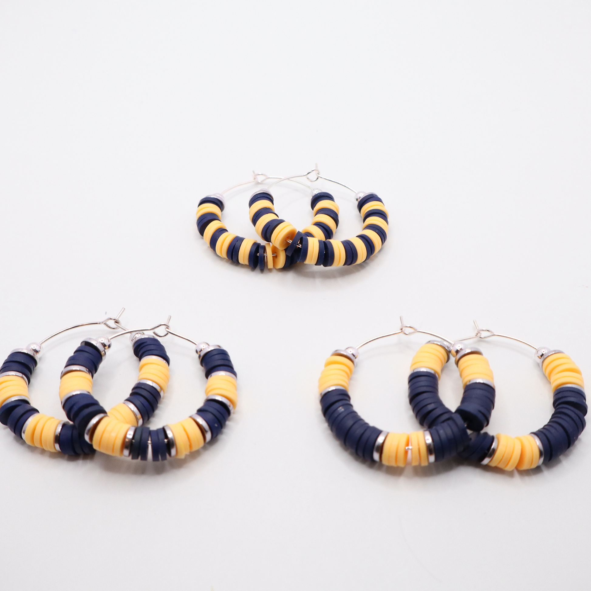 Set of three navy and gold heishi bead hoop earring styles arranged on a white background, showcasing size and pattern variations