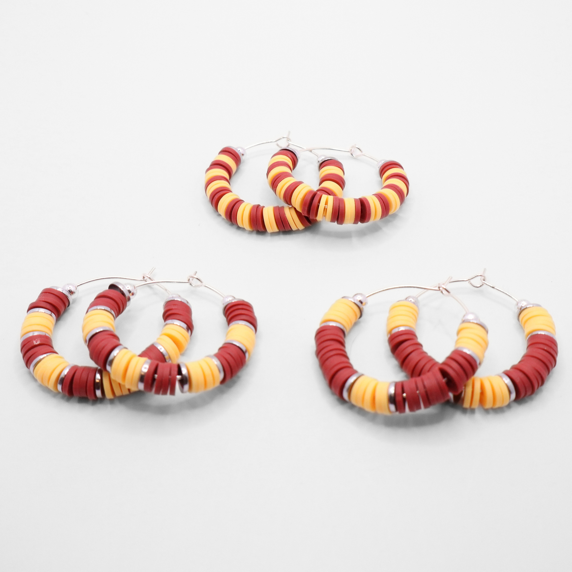 Set of three burgundy and gold heishi bead hoop earring styles arranged on a white background, showcasing size and pattern variations