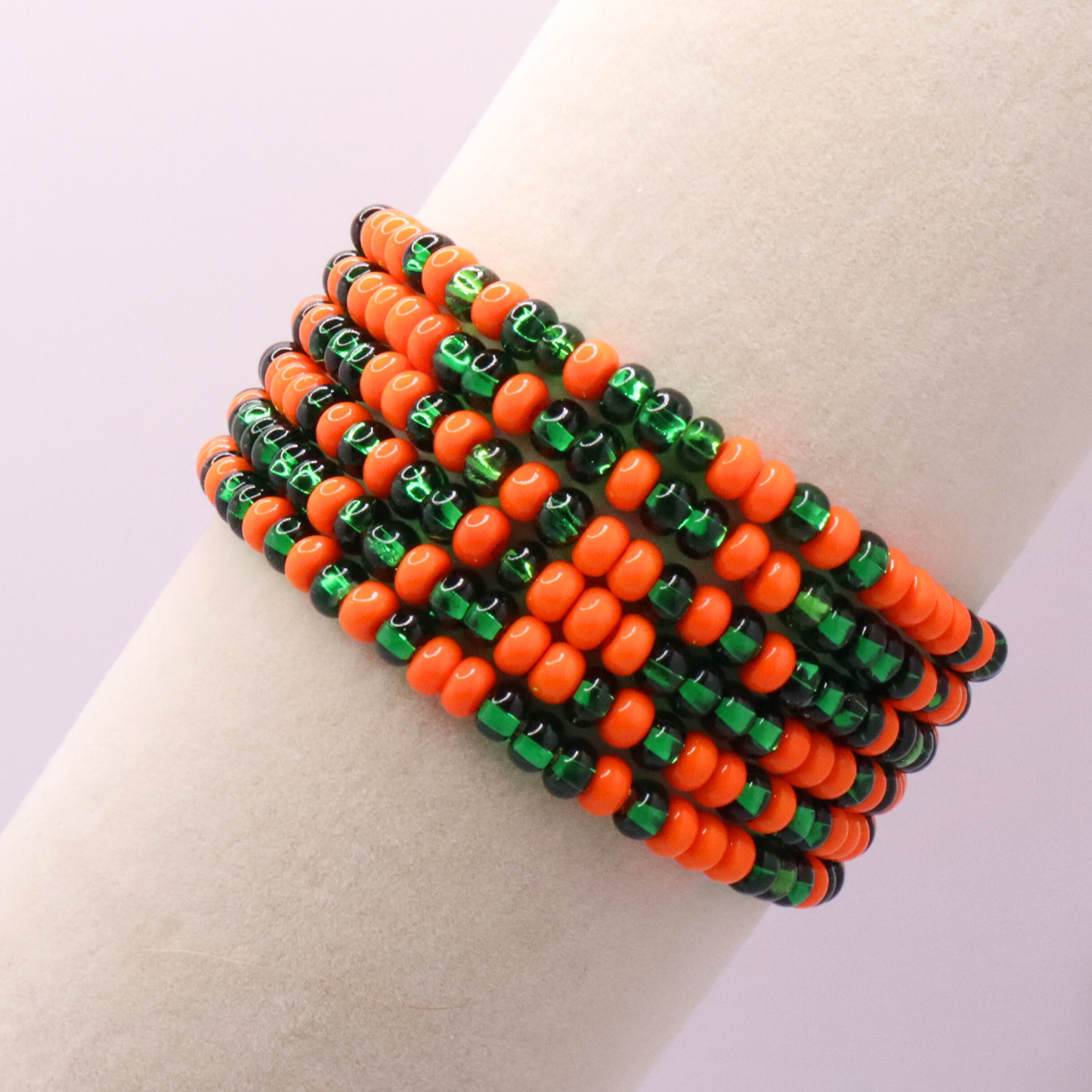 Set of six orange and green seed bead stretch bracelets featuring random orange and green seed beads on a white background