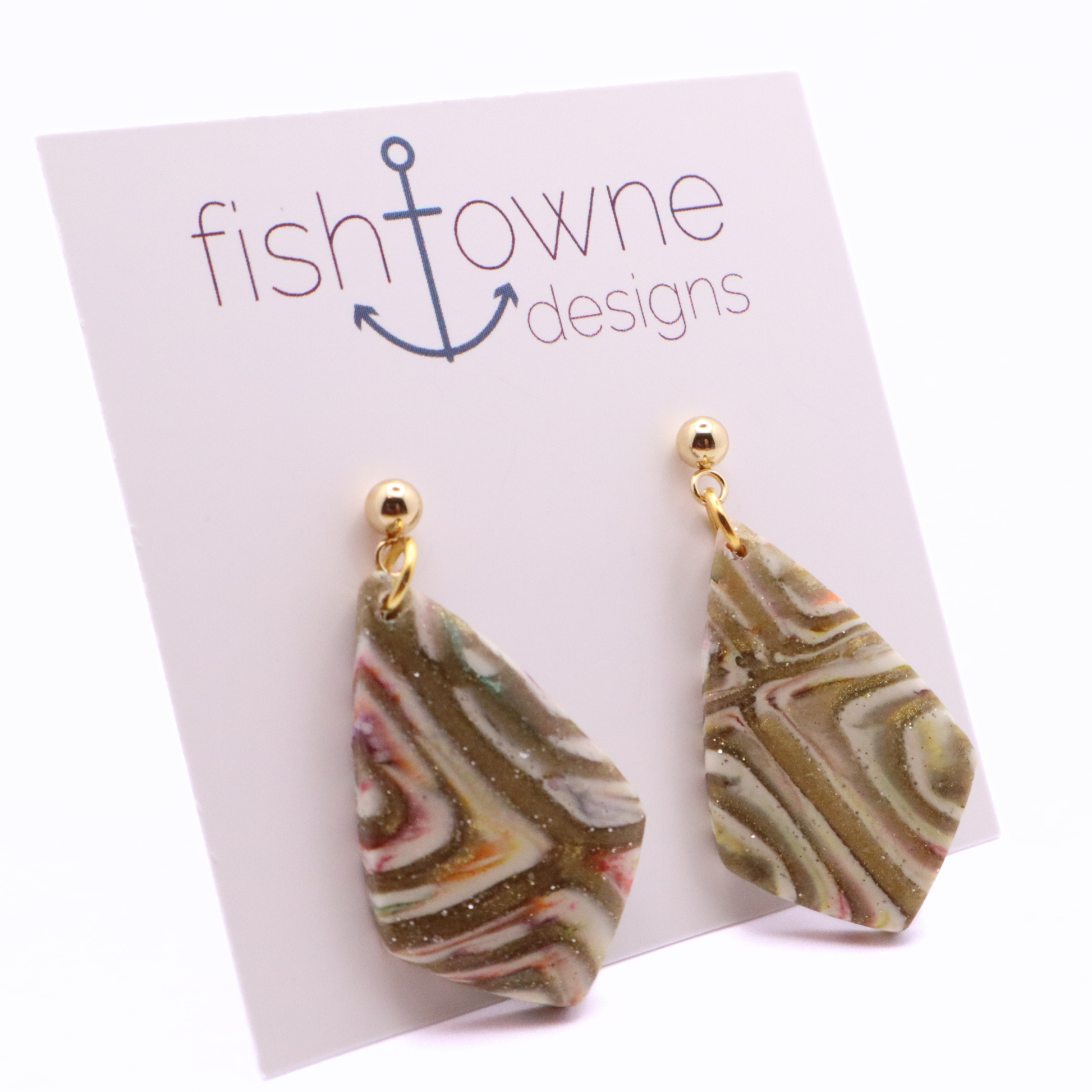 Handmade polymer clay dangle earrings with marbled neutral tones and gold shimmer on stainless steel stud posts, displayed on branded card
