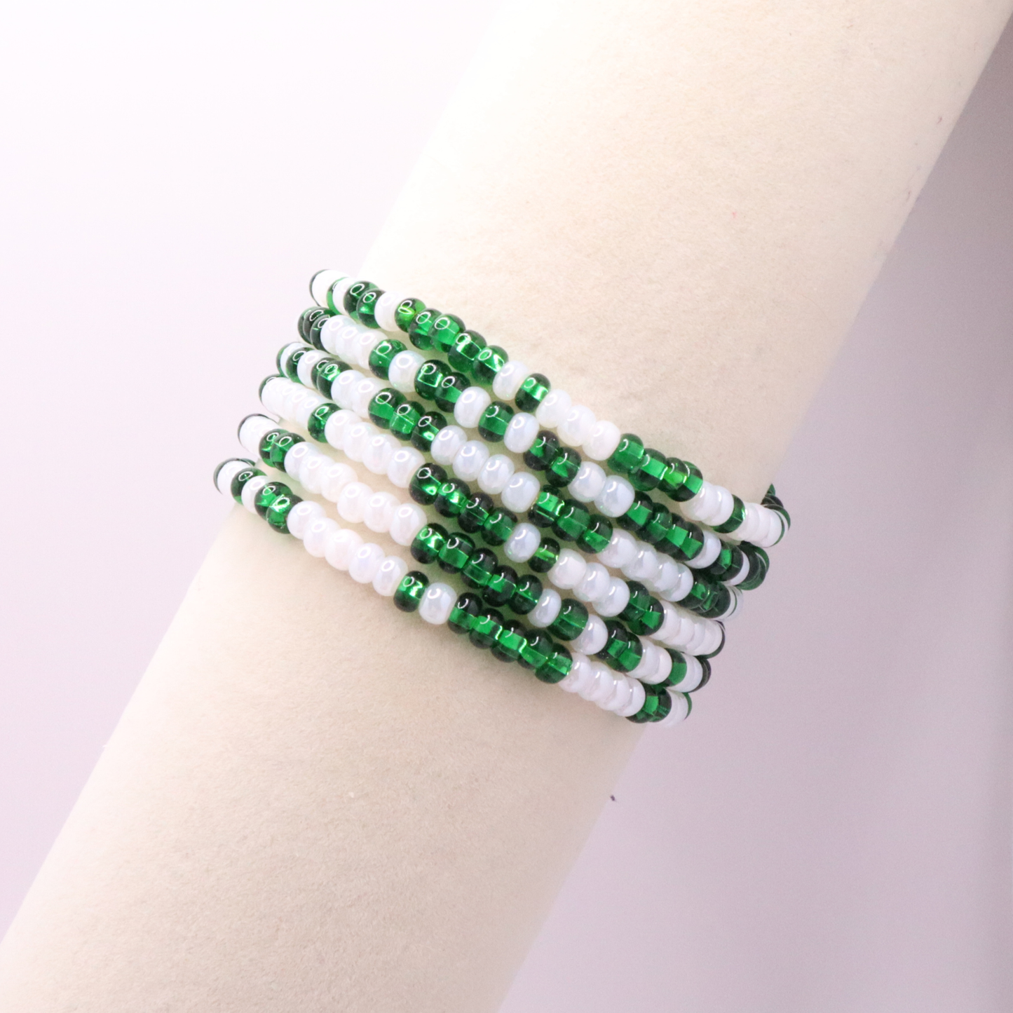 Set of six green and white seed bead stretch bracelets featuring random green and white seed beads on a white background