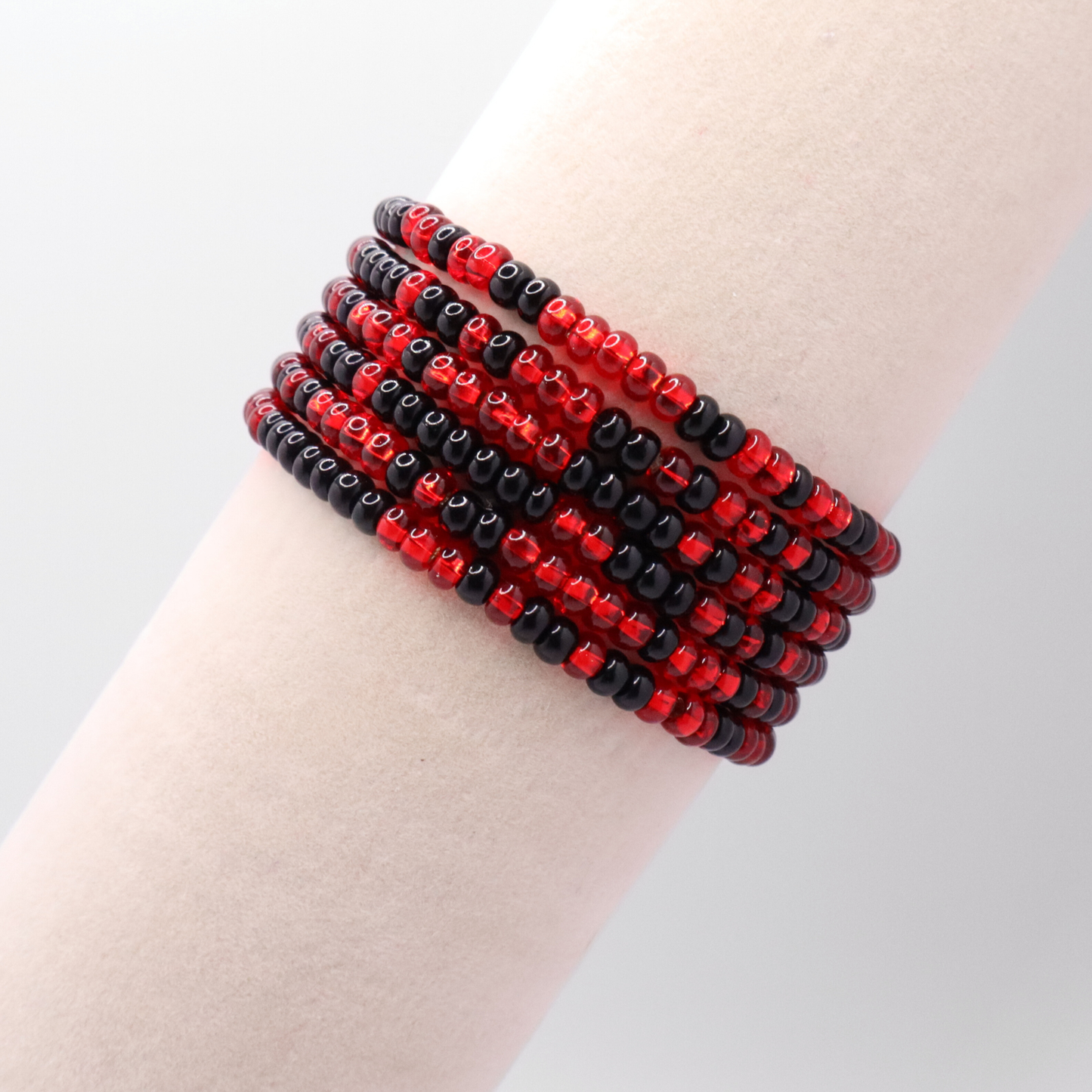 Set of six red and black seed bead stretch bracelets featuring random red and black seed beads on a white background