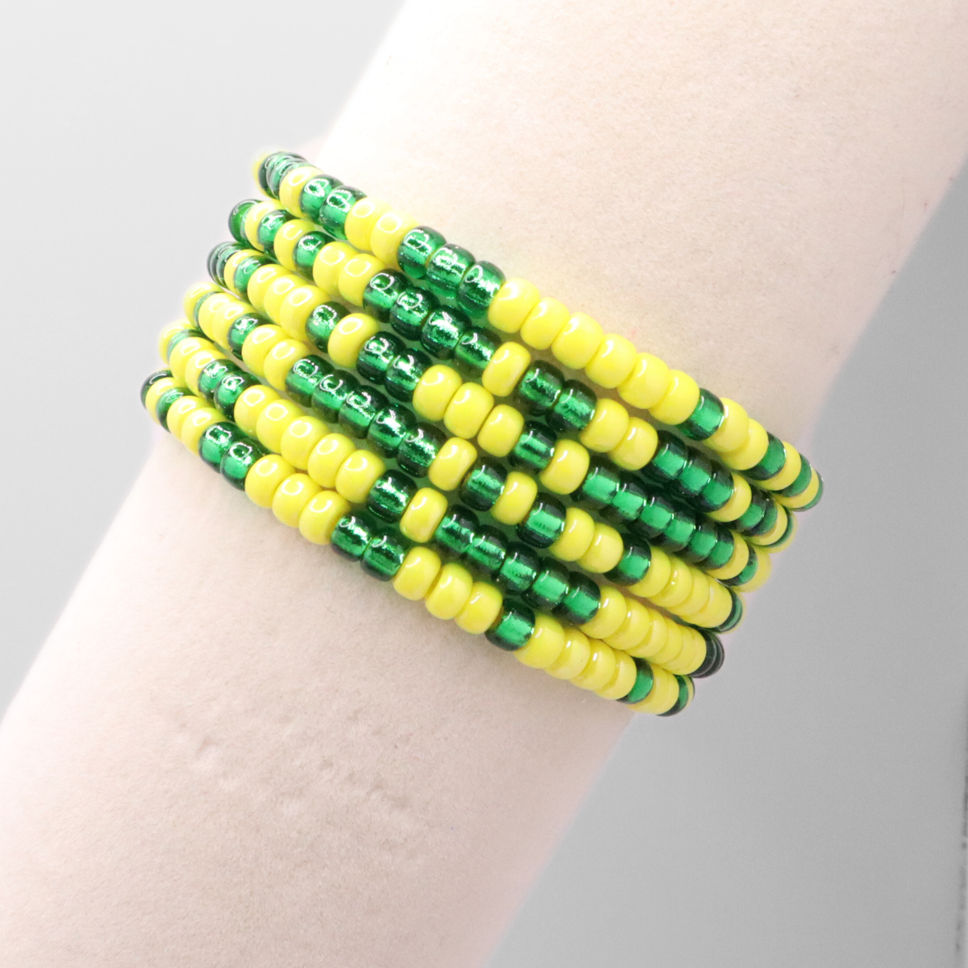 Set of six green and yellow seed bead stretch bracelets featuring random green and yellow seed beads on a white background