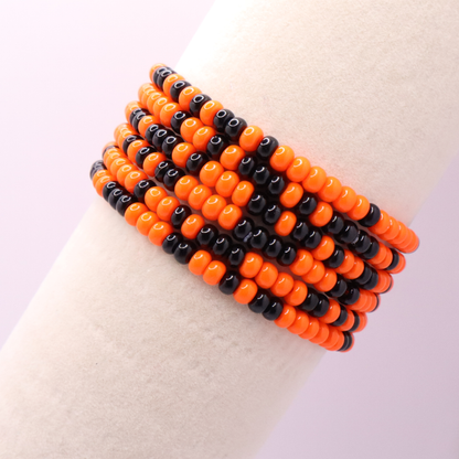 Set of six orange and black seed bead stretch bracelets featuring random orange and black seed beads on a white background