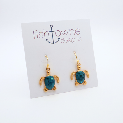 Turtle-shaped gold and teal resin earrings on a Fish Towne Designs card against a white background