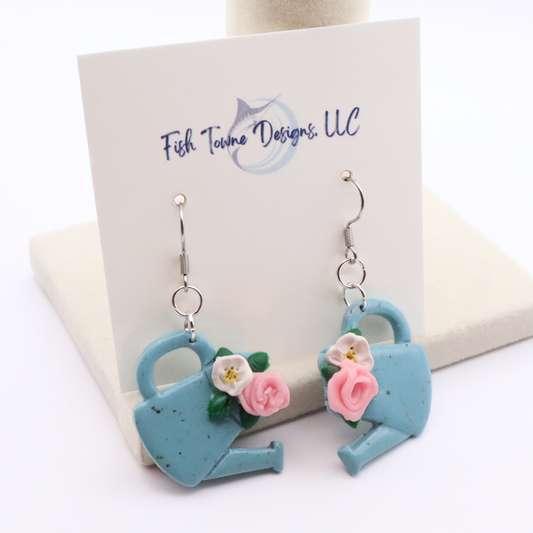 Blue watering can earrings with floral details on a Fish Town Designs card.