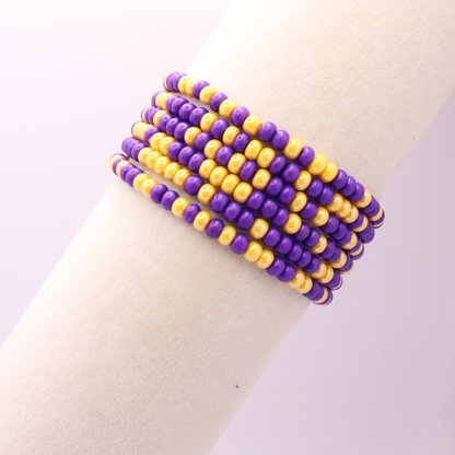 Set of six purple and gold seed bead stretch bracelets featuring random purple and gold seed beads on a white background