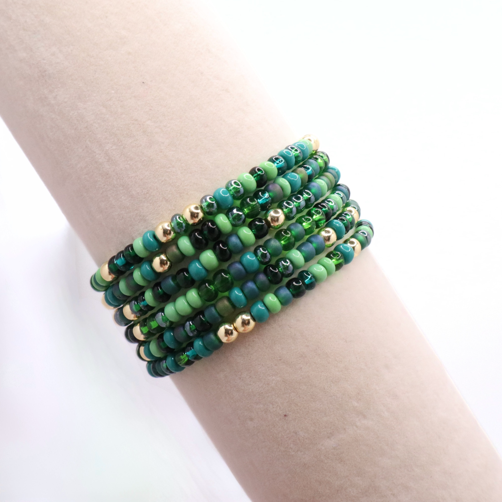 Set of six green beaded bracelet on a wrist against a white background