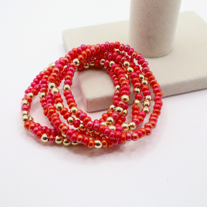 Set of six pink and gold beaded bracelets on a white surface