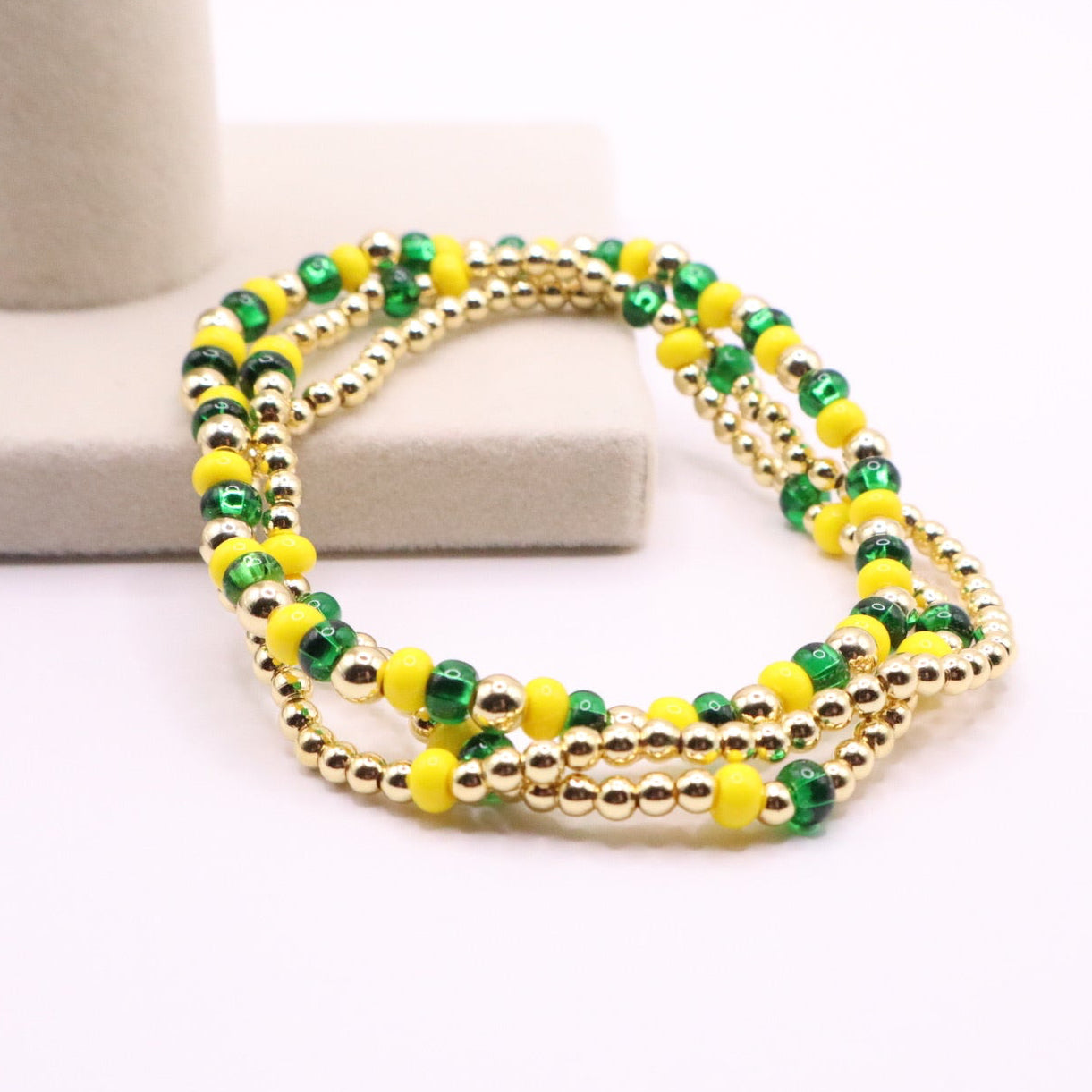 Three green, yellow, gold bracelets leaning on a beige box
