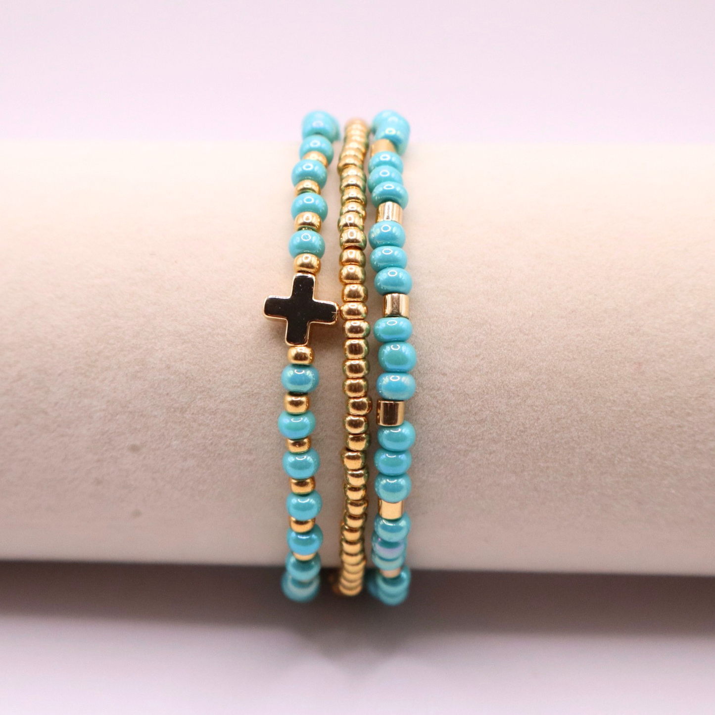 Three turquoise beaded bracelets with gold accents and a cross on a beige surface.