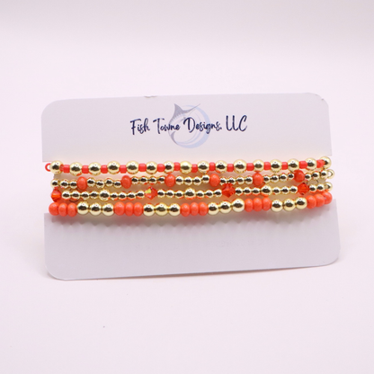 Stack of handmade stretch bracelets featuring vibrant coral Preciosa seed beads, faceted crystal accents, and polished gold-tone hematite beads on a clean white background.