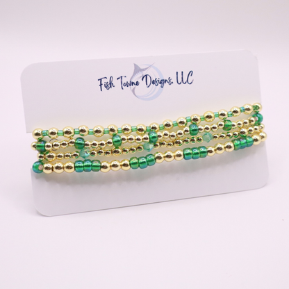 Handmade bracelet stack with green Preciosa seed beads, iridescent crystal accents, and polished gold-tone hematite beads on a clean white background.