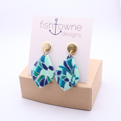 Handmade polymer clay teardrop earrings in ocean-inspired teal and blue tones with 18k gold plated studs on branded display card