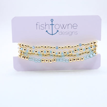 Three-piece sky blue hematite bracelet stack featuring gold-tone beads and translucent blue glass accents.